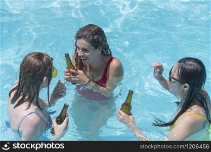 Three beautiful women holding beer bottles have fun and talk in the pool. Leisure concept.. Women having fun and talking in the pool