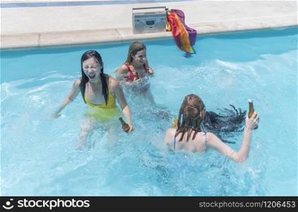 Three beautiful women laugh and have fun in the pool while holding beer bottles. Gay and diversity concept.. Group of women having fun at the pool