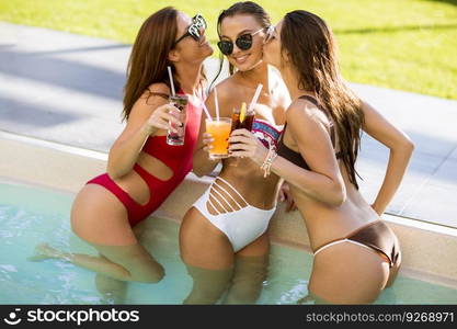 Three beautiful young woman with sun glasses drinking cocktails on the poolside of a resort swimming pool on a sunny day