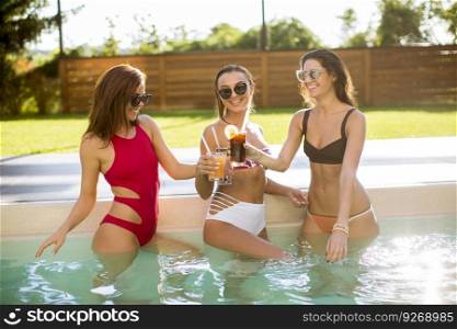 Three beautiful young woman with sun glasses drinking cocktails on the poolside of a resort swimming pool on a sunny day