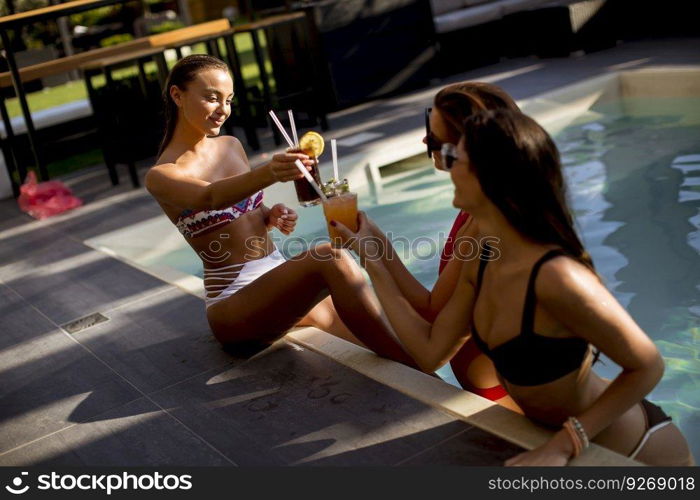 Three beautiful young woman with sun glasses drinking cocktails on the poolside of a resort swimming pool on a sunny day