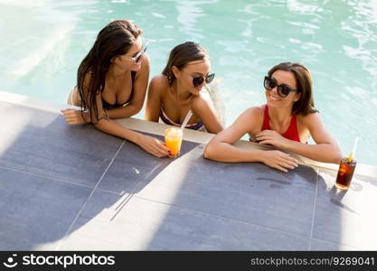 Three beautiful young woman with sun glasses drinking cocktails on the poolside of a resort swimming pool on a sunny day