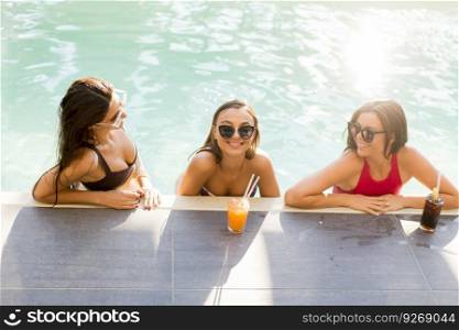 Three beautiful young woman with sun glasses drinking cocktails on the poolside of a resort swimming pool on a sunny day