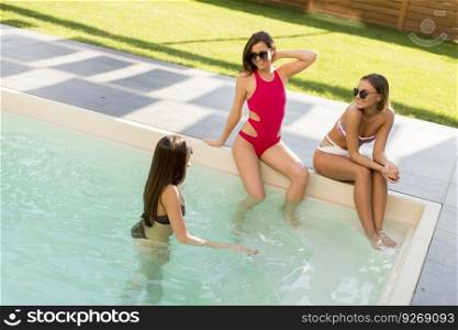 Three beautiful young woman with sun glasses sitting on  poolside of a resort swimming pool on a sunny day