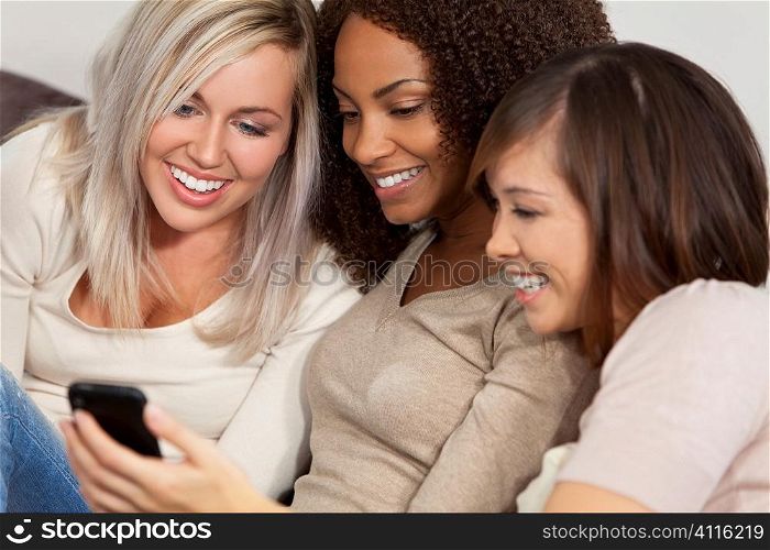Three beautiful young women having fun looking at something funny on their smart cell phone and laughing