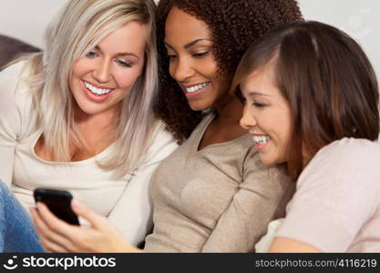 Three beautiful young women having fun looking at something funny on their smart cell phone and laughing