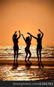 Three beautiful young women in bikinis dancing on a beach at sunset all in silhouette