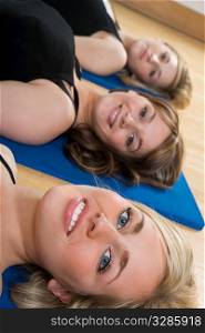 Three beautiful young women laying down on mats at a fitness class
