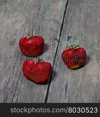 three big strawberries on a wooden table, a berry subject