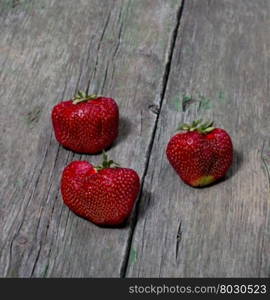 three big strawberries on a wooden table, a berry subject