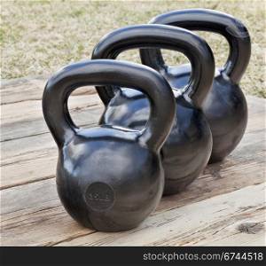 three black iron kettlebell for weight training (35 and 50 lb) on wood grunge deck, outdoors with sky reflections