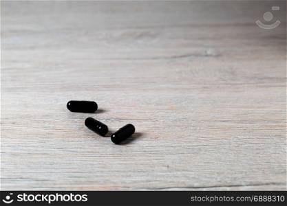 Three black medicine capsules on bright table. Three black medicine capsules on bright background