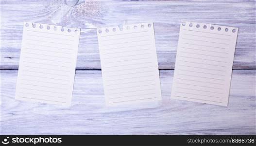 Three blank paper sheets in a line torn from a notepad on a white wooden background