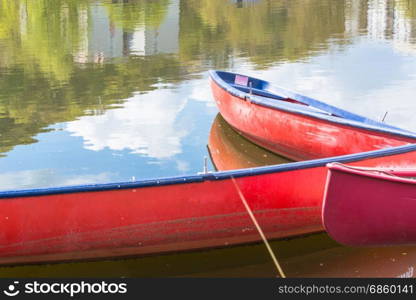 Three blank red canoes lie in the river secured to a jetty on the shore.