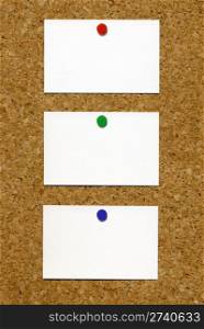 Three blank white business cards attached to a cork notice board.