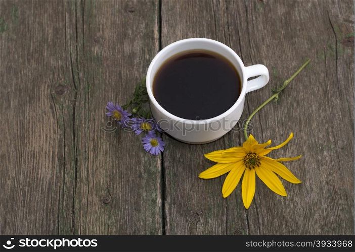 three blue flowers, one yellow and a cup of coffee on a wooden table, a still life on a subject drinks