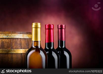 Three bottles of wine and wooden barrel on a burgundy background. Wine and barrel