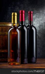 Three bottles of wine near wooden barrel in cellar. Three bottles in cellar