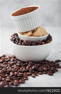 Three bowls on top of each other with fresh raw coffee beans and powder with cane sugar on light table background.