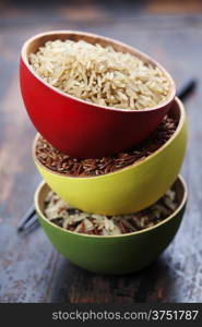 Three bowls with different types of rice on wooden background
