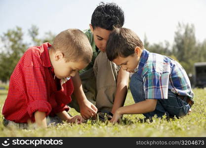 Three boys crouching on the lawn and looking down