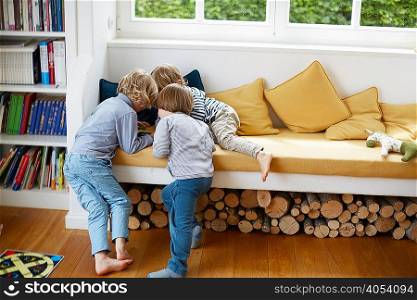 Three boys in a huddle on window seat playing