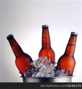 Three brown beer bottles in ice bucket with condensation