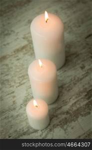Three burning Christmas candles on a white wooden background