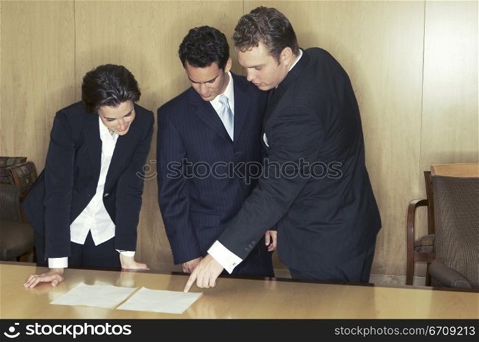 Three business people meet in the board room and discuss the documents on the conference table