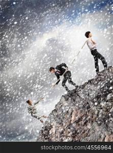 Three business people pulling rope. Image of three businesspeople pulling rope atop of mountain under falling snow