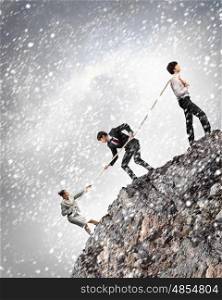 Three business people pulling rope. Image of three businesspeople pulling rope atop of mountain under falling snow