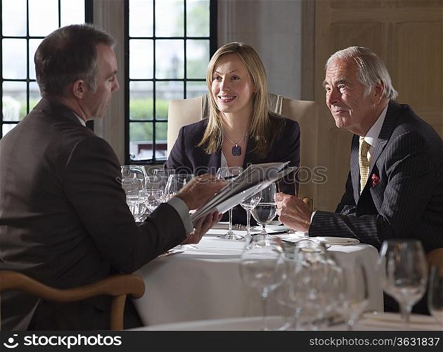 Three business people sitting at restaurant table one man holding documents