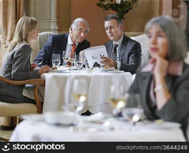 Three business people sitting at table in restaurant analyzing documents