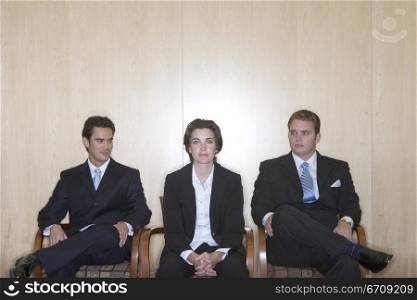 Three business people sitting with the business woman sitting in the middle and the two business men looking at her