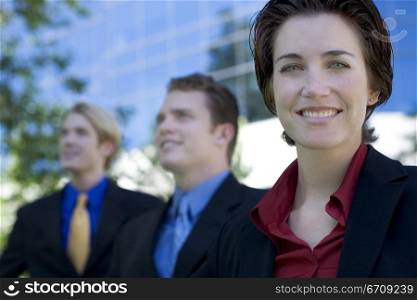 Three business people stand together while the businesswoman smiles and looks ahead