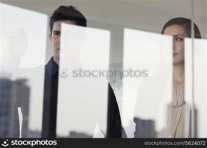 Three business people standing and looking out on the other side of a glass wall