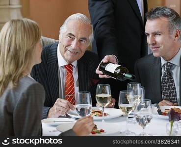 Three business people talking at restaurant table waiter serving wine