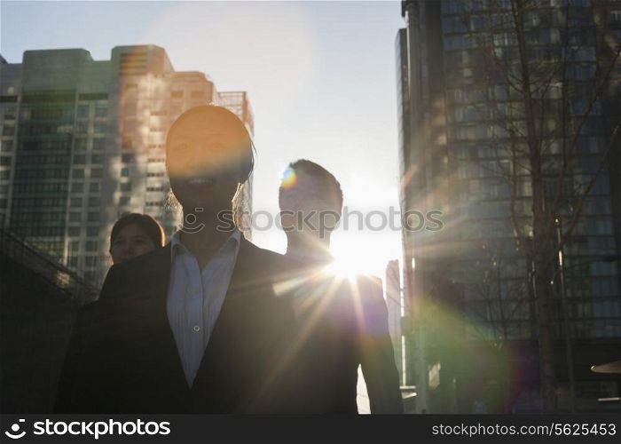 Three business people walking down a city street with sunlight at their back, lens flare