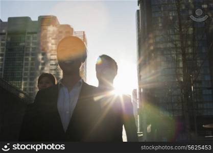 Three business people walking down a city street with sunlight at their back, lens flare