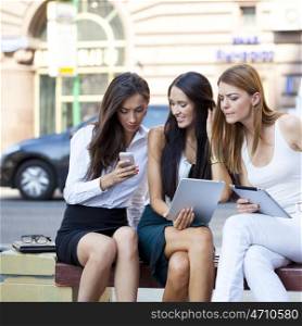 Three business women sitting on a bench in the summer city