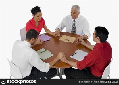 Three businessmen and a businesswoman praying with holding their hands in a meeting