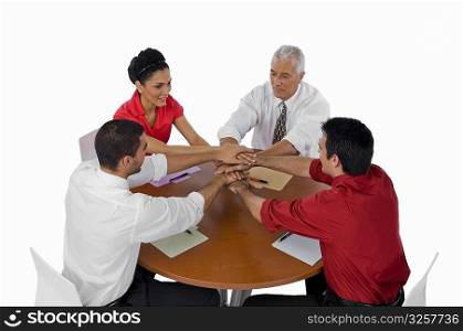 Three businessmen and a businesswoman stacking hands on top of each other in a meeting