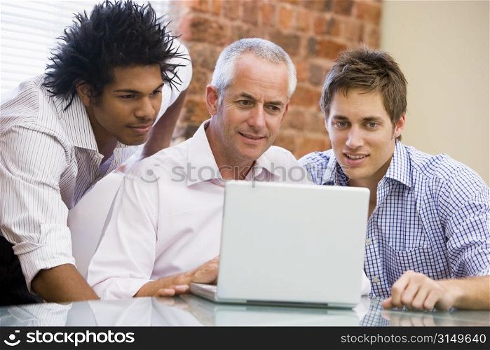 Three businessmen in office looking at laptop smiling