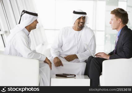 Three businessmen indoors with a laptop talking and smiling (high key/selective focus)