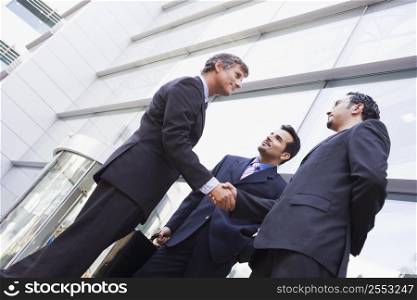 Three businessmen outdoors by building shaking hands and smiling (high key/selective focus)