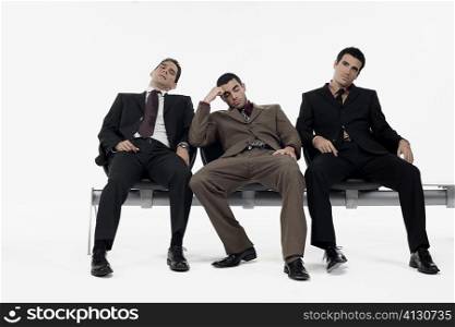 Three businessmen sitting a bench and looking stressed
