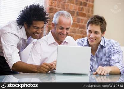 Three businessmen sitting in office with laptop smiling