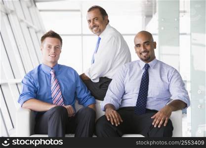 Three businessmen sitting indoors smiling (high key/selective focus)