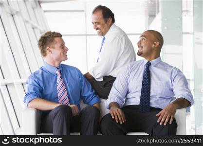 Three businessmen sitting indoors smiling (high key/selective focus)