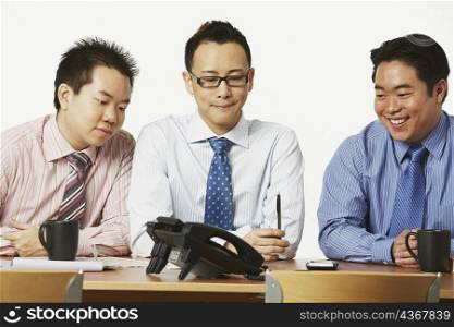 Three businessmen sitting on chairs looking at the telephone